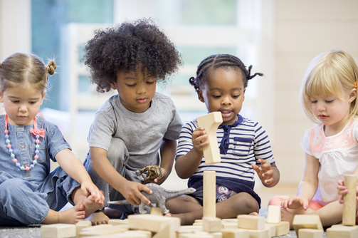 A diverse group of young children sitting on the ground together playing with blocks